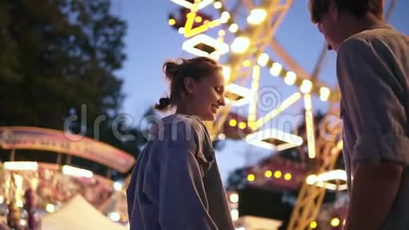 年轻夫妇约会在游乐园见面男人给她女朋友带了一颗棉花糖接吻明亮的灯光视频的预览图