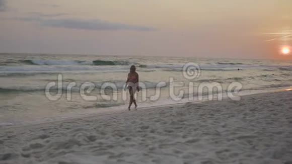 4k日落时在沙滩上沿着海浪散步的时髦孕妇视频的预览图