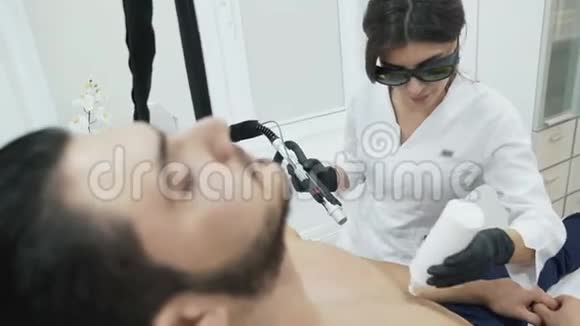 一位美丽年轻的美容师在男性病人的胃上涂上扩张凝胶把这个装置拿进去视频的预览图