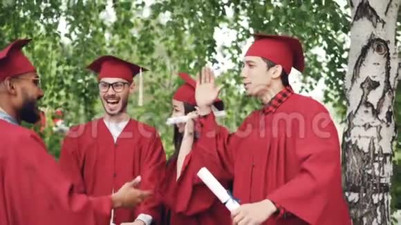 兴奋的年轻男女毕业生们正在高举着庆祝毕业证书拥抱和欢笑视频的预览图