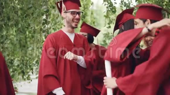 快乐的毕业生穿着长袍和灰泥板拥抱欢笑和祝贺对方的缓慢动作视频的预览图
