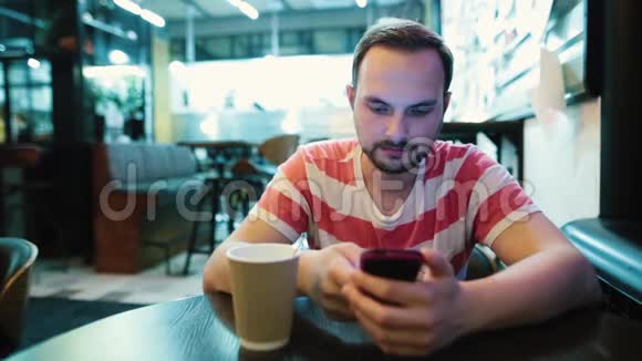 有胡子的年轻帅哥在咖啡馆里用智能手机视频的预览图