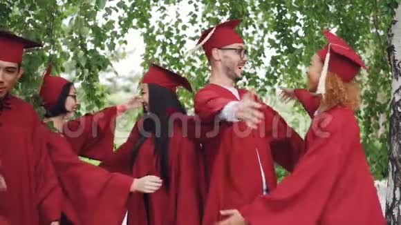 兴奋的年轻人毕业时穿着长袍戴着帽子拥抱着互相祝贺视频的预览图