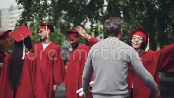 自豪的父母拥抱他成功的女儿站在校园户外庆祝毕业日视频的预览图