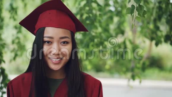 站在校园里微笑着身着长袍和灰泥板的亚洲女毕业生慢镜头画像视频的预览图