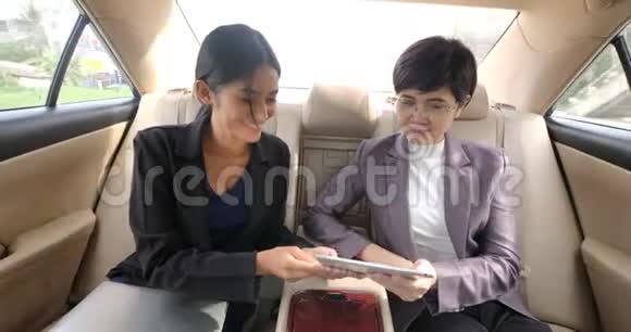 两个女商人坐在汽车后座上拿着数字平板电脑说话视频的预览图