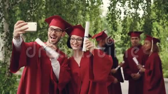 一对即将毕业的学生正在用智能手机自拍年轻的男女都拿着文凭视频的预览图
