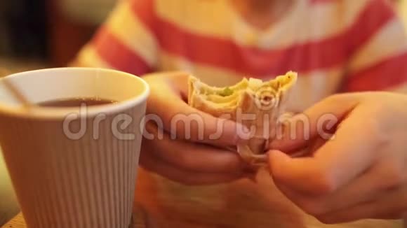 年轻的白种人在皮塔面包里吃美味的沙瓦玛喝茶或咖啡坐在咖啡馆里特写镜头视频的预览图