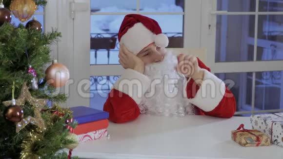 无聊的圣诞老人坐在桌子旁玩着红帽子视频的预览图