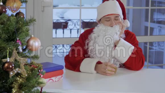 穿着圣诞老人西装留着假胡子的年轻人坐在餐桌旁喝酒视频的预览图