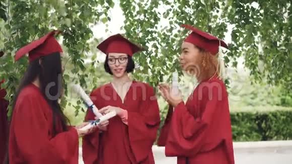 三位漂亮的女毕业生在毕业典礼上交谈并持有毕业证书学生们感到骄傲和兴奋视频的预览图