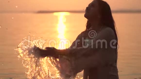 一个迷人的年轻女孩在阳光的映衬下双手在水中挥出一朵美丽的浪花视频的预览图