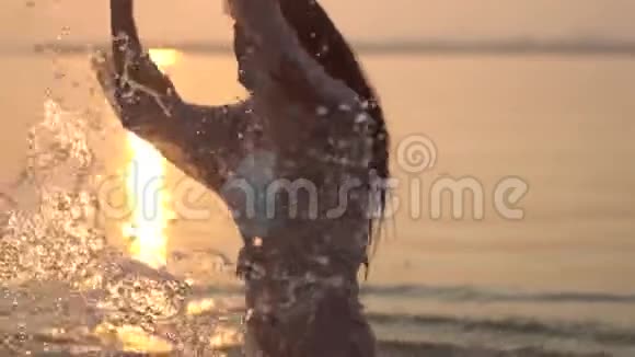 迷人的年轻女孩在阳光的映衬下双手在水中飞溅慢动作高清高清视频的预览图