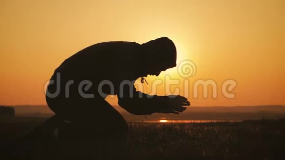 剪影的年轻人在美丽的夕阳下在外面祈祷男性寻求帮助在信仰概念宗教中找到慰藉视频的预览图
