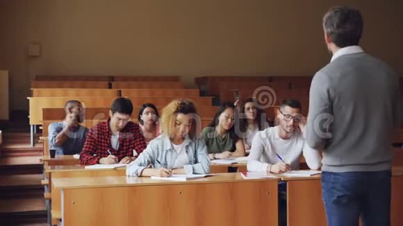 教师正在宽敞的大学报告厅与坐在课桌前的学生交谈穿着便服的年轻人视频的预览图