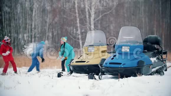 冬季森林一家人穿着五颜六色的衣服在雪地摩托附近玩雪球慢动作视频的预览图