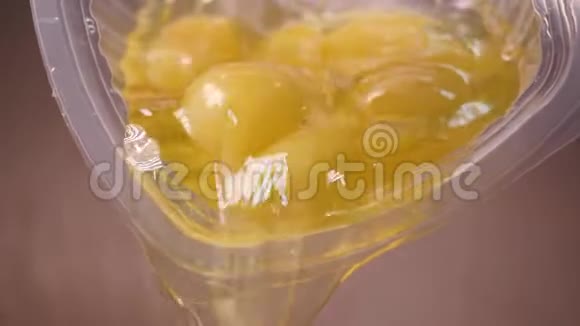 从杯子里倒入的生鸡蛋的特写库存录像含有蛋黄和蛋白质的生鸡蛋从塑料容器中扩散视频的预览图