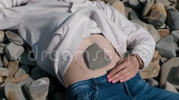 石头在女孩肚子上秋天躺在石滩上的面目全非的女孩视频的预览图