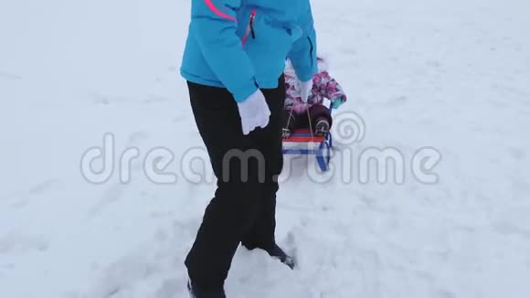 在冬天年轻的母亲在雪道上雪橇上滚动小婴儿孩子顽皮坐在雪橇上哭泣视频的预览图