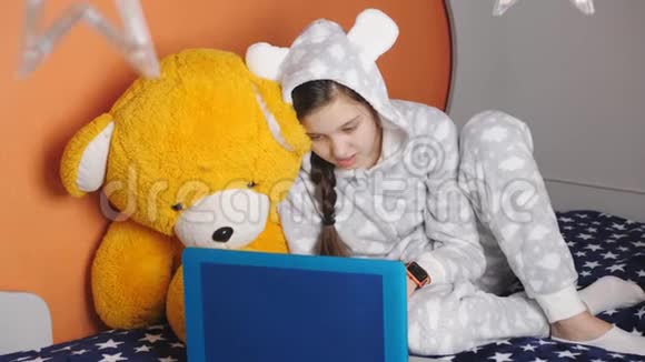 少女穿着温暖的睡衣躺在床上通过笔记本电脑上的互联网视频的预览图