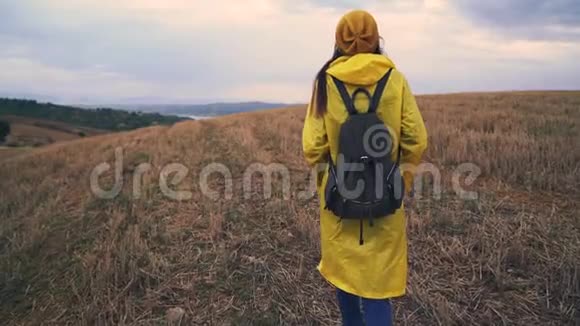 在田里散步的旅行者女人穿着黄色雨衣背包的女孩视频的预览图