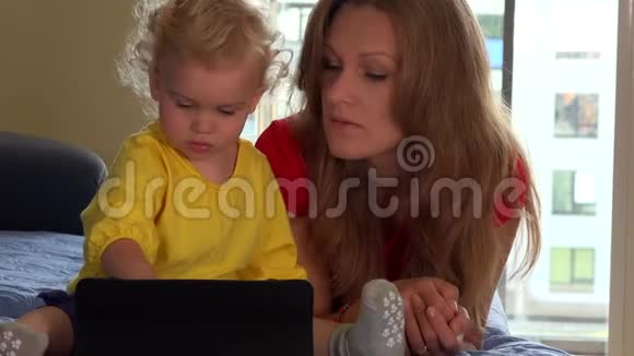 微笑的母亲和她可爱的蹒跚学步的女儿在家里使用平板电脑视频的预览图