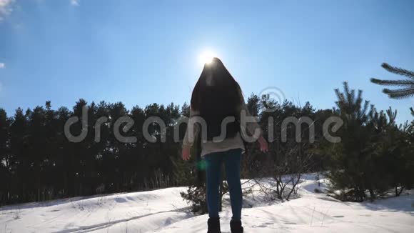年轻的女孩站在冬天森林的背景上举起她的手臂女人享受冬天的风景自由视频的预览图