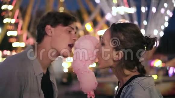 游乐园里可爱的年轻夫妇花时间在一起从侧面吃粉红色的棉花糖可爱的一对视频的预览图