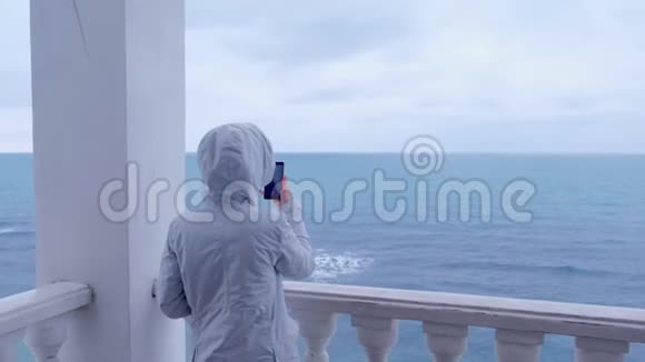 穿着白色夹克的女人在美丽的露台上拍摄海浪视频后景视频的预览图