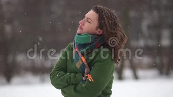 美丽的年轻女子享受着降雪无所畏惧穿着绿色外套和围巾冬天在公园散步视频的预览图