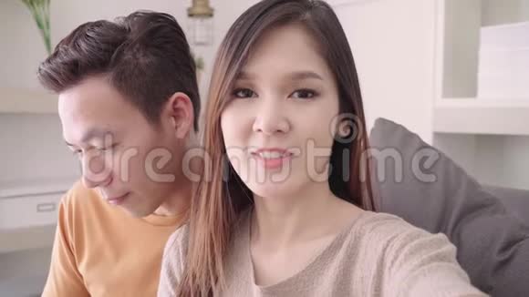 亚洲夫妇使用智能手机视频电话与朋友在客厅在家里视频的预览图