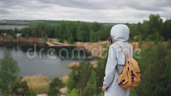 倾斜的慢镜头描绘了一个苗条的女孩背对着镜头走在悬崖上看着美丽的风景视频的预览图