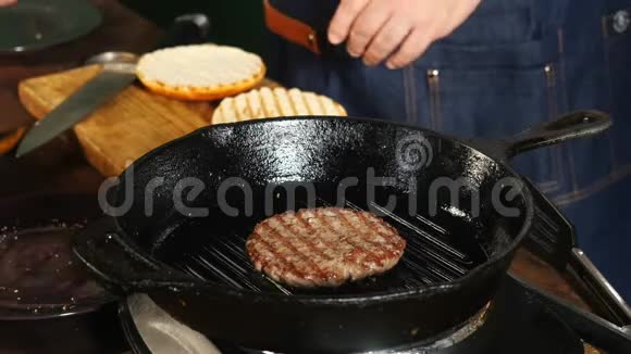 男厨师穿着蓝色围裙在平底锅烤架上煎切片靠近其他制作汉堡包的原料库存数据视频的预览图
