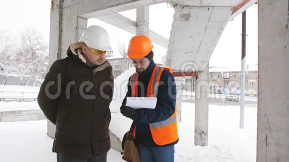 一名工程师和主管讨论冬季在一个下雪的建筑工地上的施工计划视频的预览图