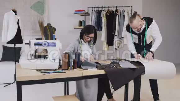 团队合作英俊的裁缝或时装设计师在他的工作室工作在织物上绘制模板创作一部作品视频的预览图