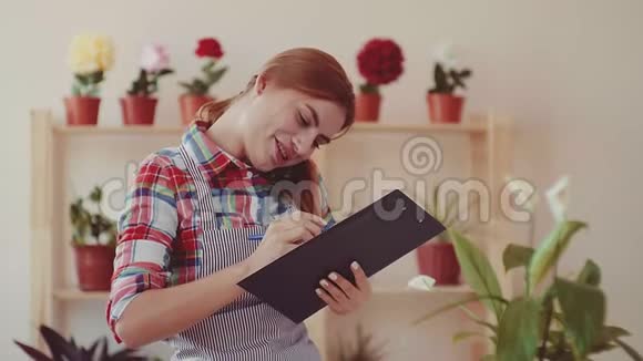 小生意开一家花店一个女孩穿着格子衬衫和一条条纹围裙手里拿着一张纸微笑着视频的预览图