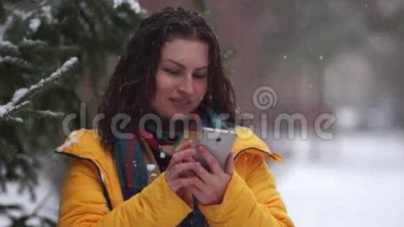 在公园玩滚雪球的时候一个棕色卷发的女人那个女孩拿到雪球时拿着手机冬季运动会视频的预览图
