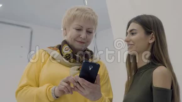 成熟的女人向她的同事展示智能手机上的照片视频的预览图
