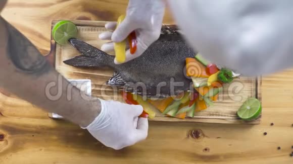 厨师在木制背景上用新鲜蔬菜装饰炸鱼食品设计与造型理念烤鱼视频的预览图