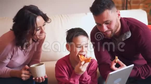 在客厅里吃披萨的同时使用数码平板电脑的幸福家庭视频的预览图