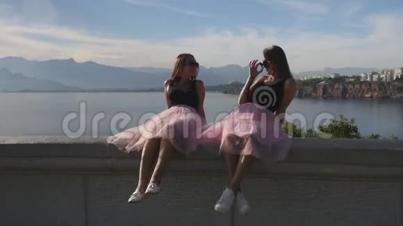 两个穿着薄纱裙和运动鞋坐在海边的年轻美女视频的预览图