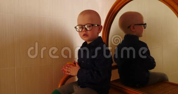 小金发男孩坐在梳妆台上带着镜子吃了一个橘子这孩子在家玩得很开心视频的预览图