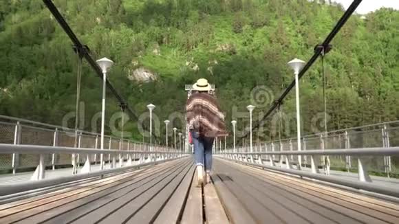 那个穿着斗篷和草帽的女人沿着斜拉桥穿过山河视频的预览图