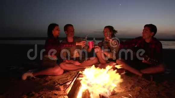 一群人晚上在海滩上的篝火旁消磨时间喝酒干杯年轻人抱着视频的预览图