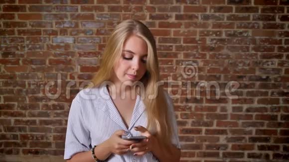 年轻的白种人金发美女使用智能手机显示智能手机屏幕绿色屏幕肖像砖墙视频的预览图