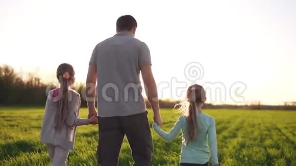 年轻肌肉发达的男人父亲用手牵着他的小女儿走在宽阔的草地旁休闲服太阳视频的预览图