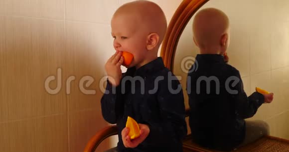 小金发男孩坐在梳妆台上带着镜子吃了一个橘子这孩子在家玩得很开心视频的预览图