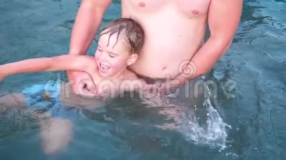 一位年轻的爸爸和他的孩子在炎热的夏天在一个小湖里游泳这孩子非常快乐和快乐花园鲜花视频的预览图