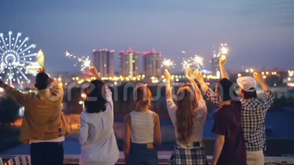 快乐的青年朋友们慢悠悠地举着星星之火举起双手站在屋顶上欣赏美景视频的预览图
