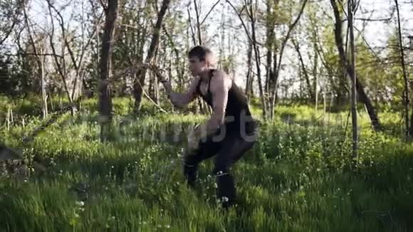 一名运动男性使用战绳锻炼身体的侧视克罗斯菲特荡秋千绿色公园黑色运动服视频的预览图